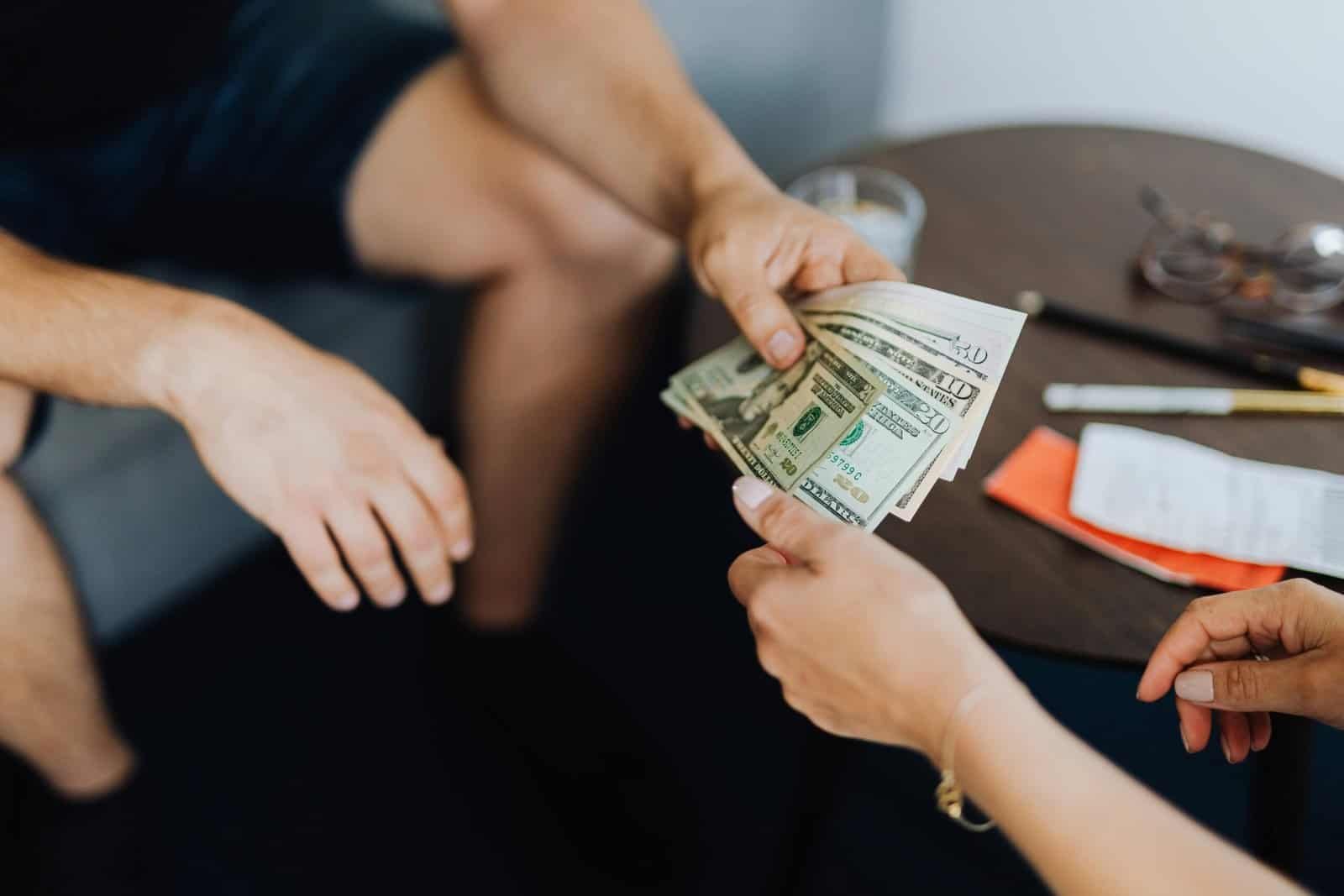 Close-up of hands exchanging US dollar bills, symbolizing a financial transaction or payment.